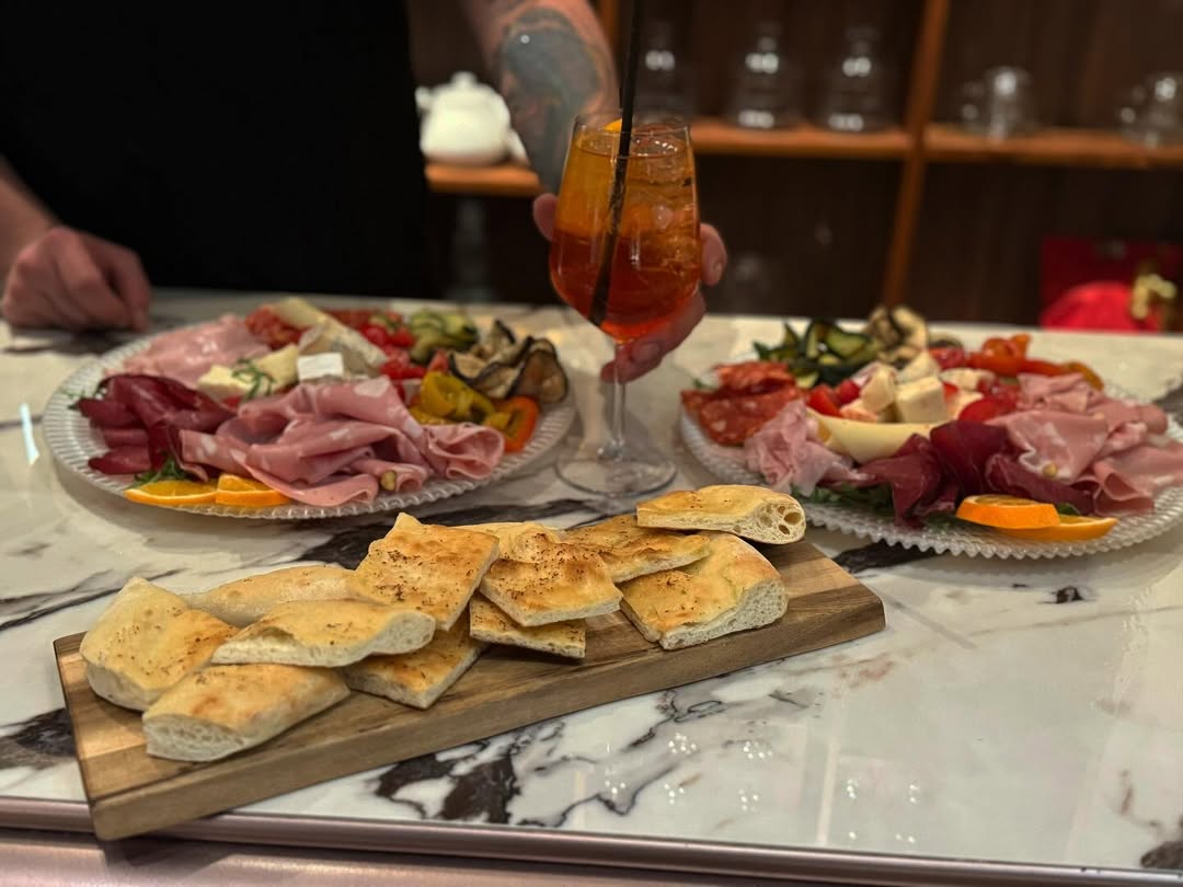 Spritz servito con taglieri di salumi e focaccia sul bancone in marmo